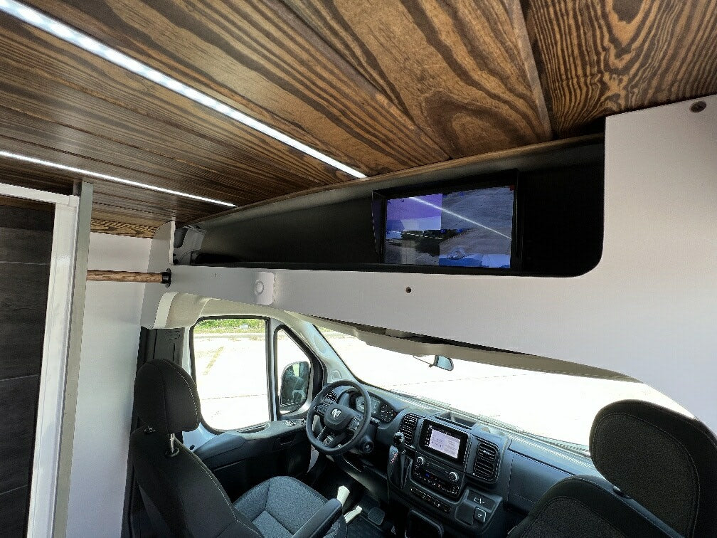 View inside a sleek rv rental camper van. Features a wood ceiling with LED lights, front cab, dashboard, and an overhead screen.