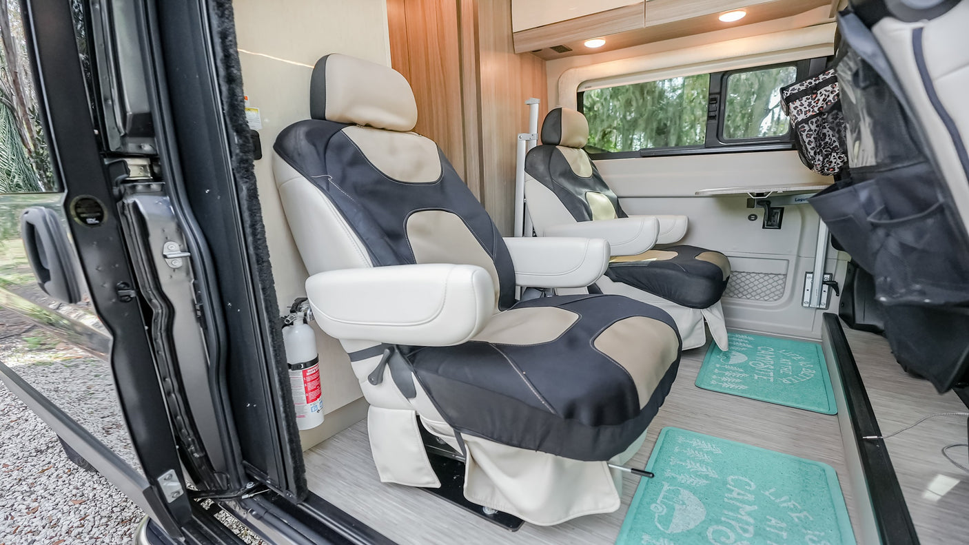 Comfortable RV rental interior with swiveling seats, a portable table, and a fire extinguisher near the door.
