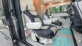 Comfortable RV rental interior with swiveling seats, a portable table, and a fire extinguisher near the door.