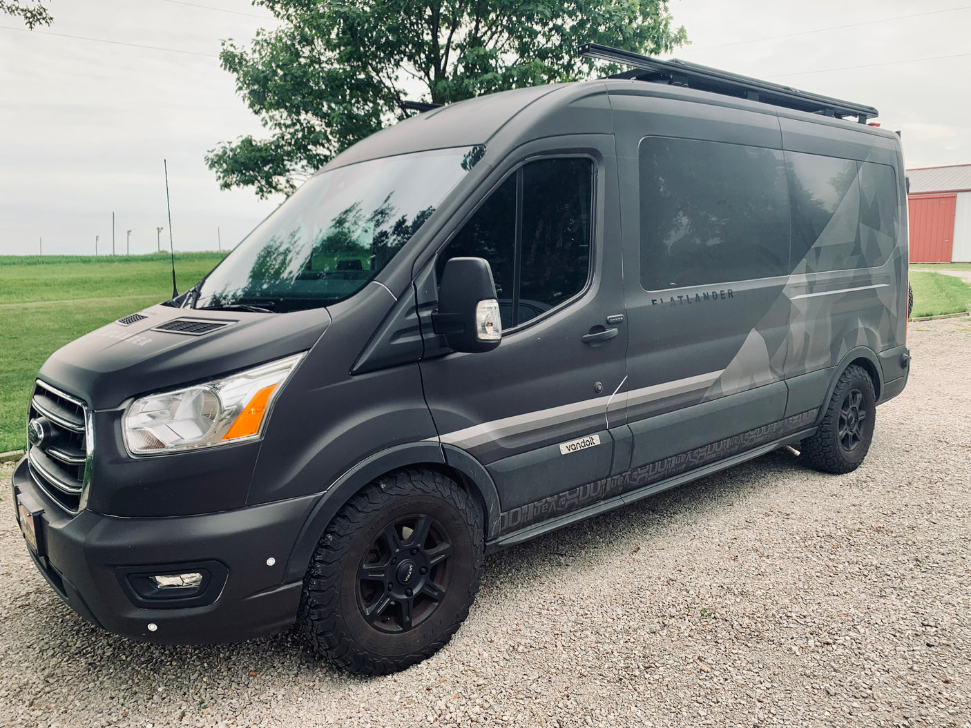 Dark gray Ford Transit Flatlander camper van by Vandoit, ideal for RV rental, parked on gravel.