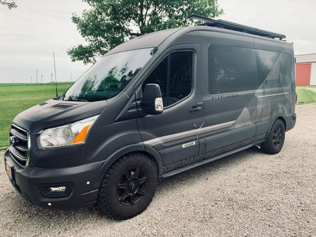 Dark gray Ford Transit Flatlander camper van by Vandoit, ideal for RV rental, parked on gravel.