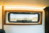 RV rental interior: A window framed in wood, white walls, and LED lighting, revealing a desert view with cacti.