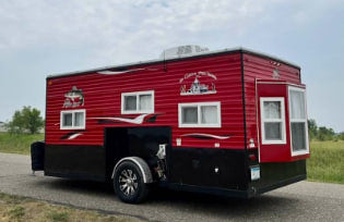 Red & black ice fishing house, a unique RV rental option for outdoor adventure. This versatile trailer features multiple windows.