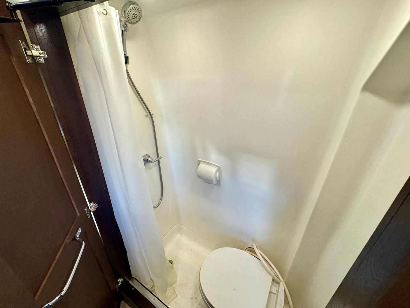 Compact RV rental wet bath with shower, toilet, and toilet paper holder. Efficient design for travel and small living spaces.