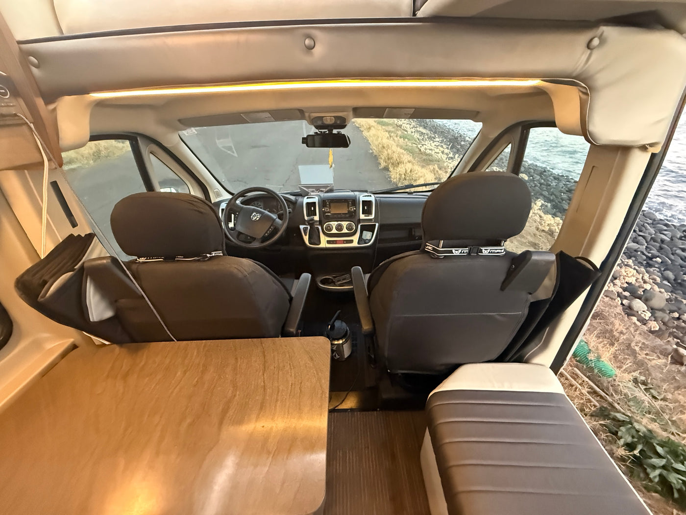 Inside an rv rental: forward view from living area, showing cockpit, steering wheel, and a scenic road & ocean outside. — photo 19