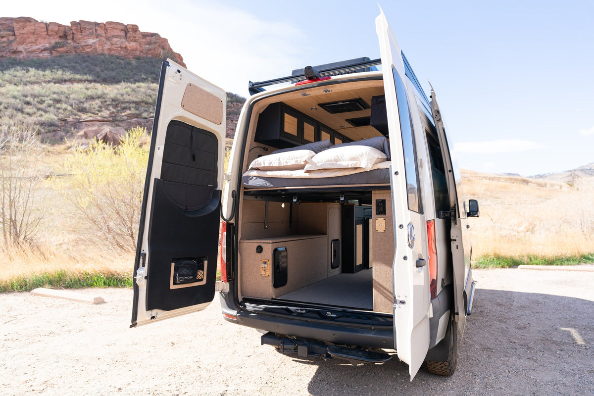 Beautiful rv rental camper van with open rear doors showing a cozy bed, storage, and custom interior in a natural setting. — photo 6
