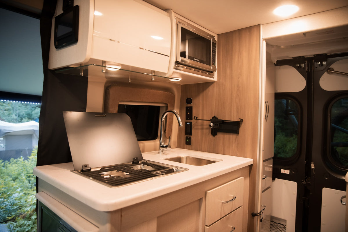 Spacious RV rental kitchen with microwave, sink, and covered stovetop, featuring modern cabinets and drawers for on-the-go cooking. — photo 11