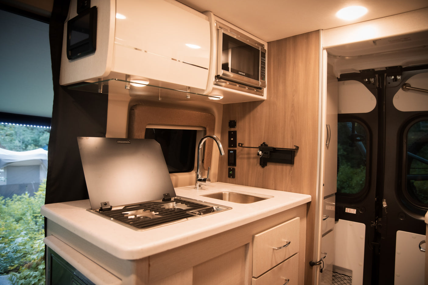 Spacious RV rental kitchen with microwave, sink, and covered stovetop, featuring modern cabinets and drawers for on-the-go cooking.