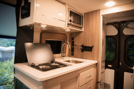 Spacious RV rental kitchen with microwave, sink, and covered stovetop, featuring modern cabinets and drawers for on-the-go cooking.