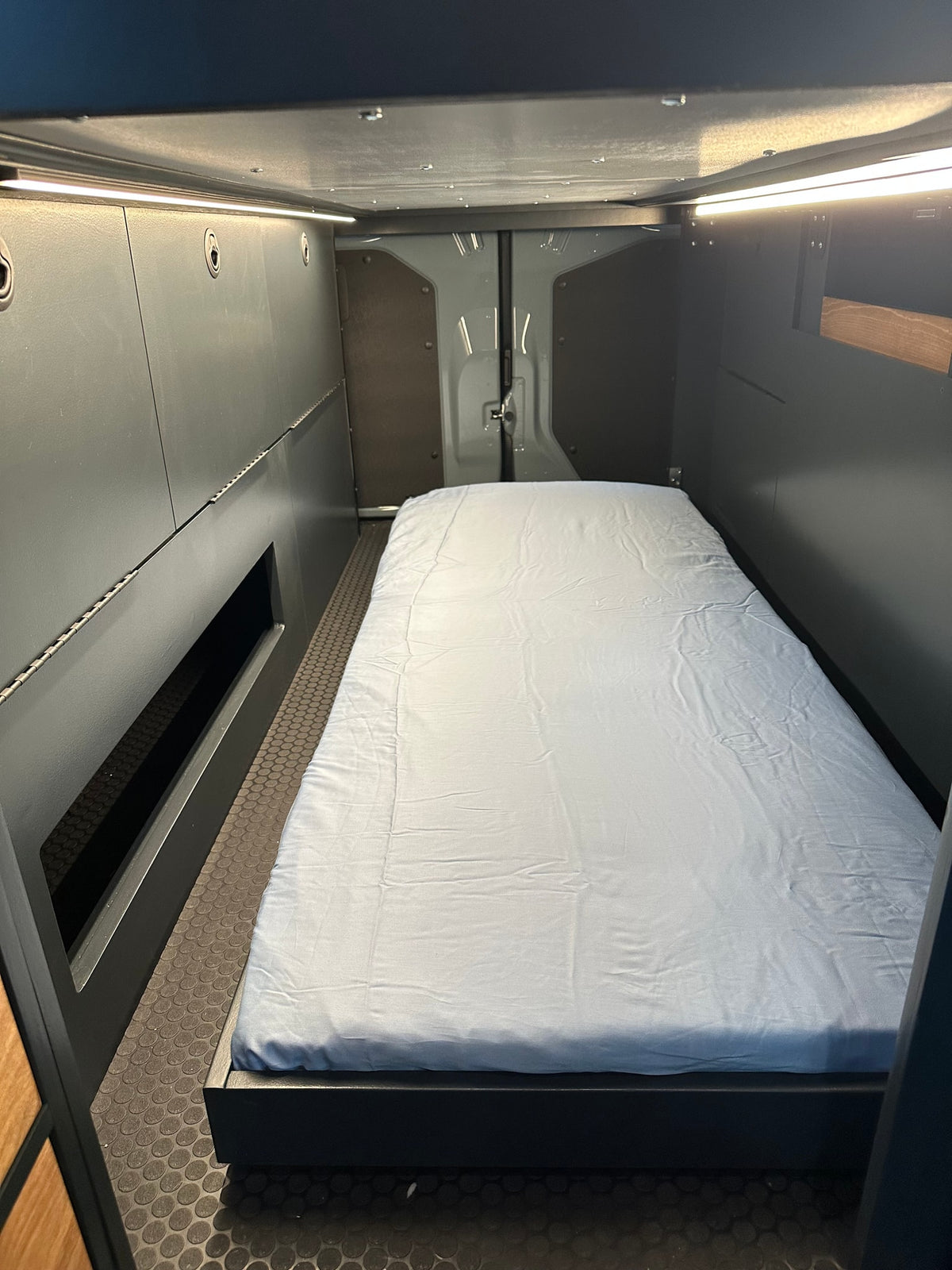 Comfortable sleeping area in a modern RV rental. Features a bed, dark walls with integrated lighting, and textured floor. — photo 3