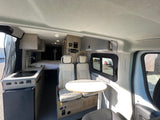 Modern rv rental interior featuring a compact kitchen, comfortable bed, and versatile seating with a table.