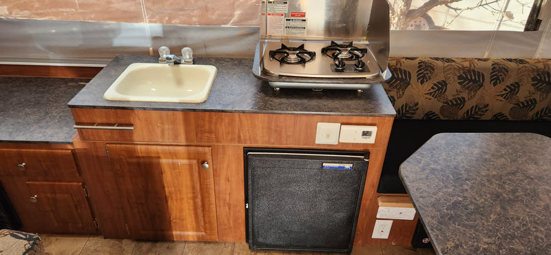 RV rental interior: Compact camper kitchen with sink, Suburban stove, Norcold fridge, and dinette area. Thermostat shows 52. — photo 6