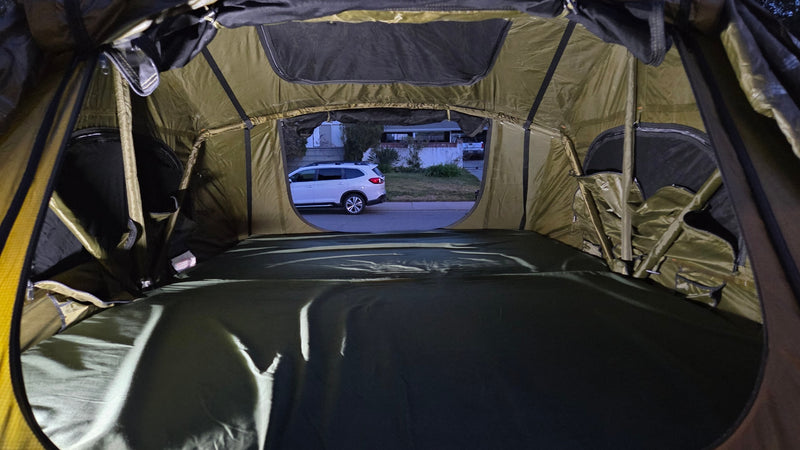 Inside a spacious RV rental rooftop tent with a mattress, looking out at an SUV parked on a quiet street at dusk. — photo 11