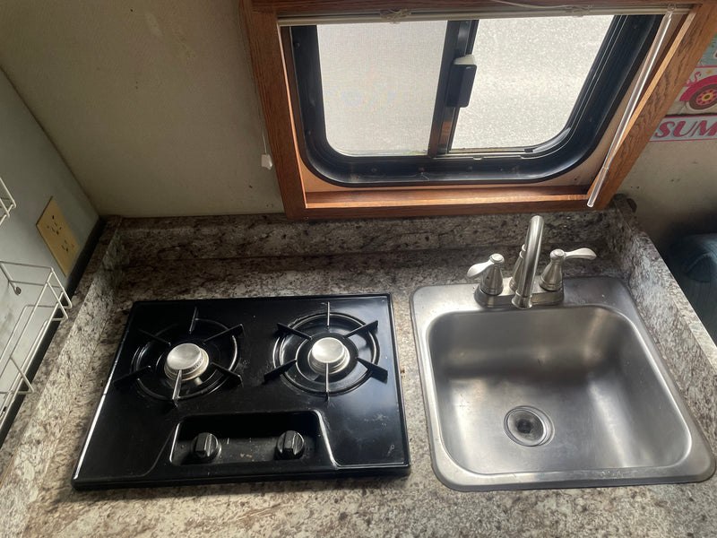 Compact RV rental kitchen featuring a two-burner stove, stainless steel sink, and a window with a screen. — photo 4