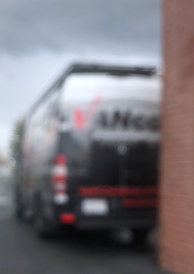 Extremely blurry black van, potentially an RV rental, parked by a brick wall. Red taillights are visible on the vehicle. — photo 11
