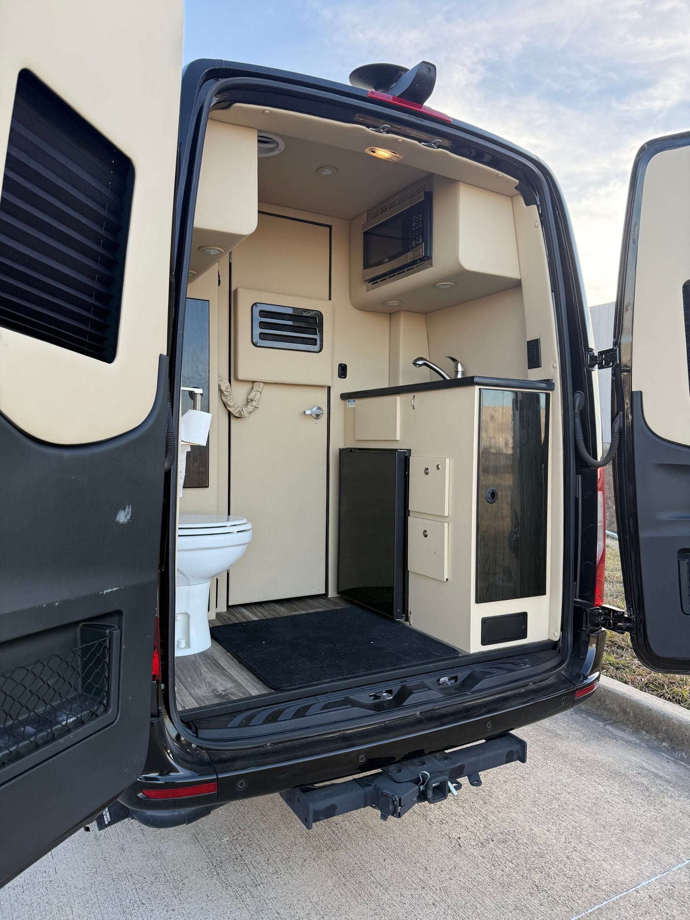 Rear view of a modern rv rental interior, showing a compact kitchen with microwave, sink, fridge, and built-in toilet. — photo 5