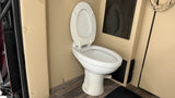 A clean white toilet with an open lid in an RV rental bathroom. Features beige walls, wood-look floor, and dark accents.
