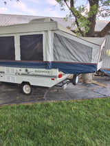 Rockwood Premier pop-up RV rental set up outdoors, nestled beside a tree on black landscape fabric.