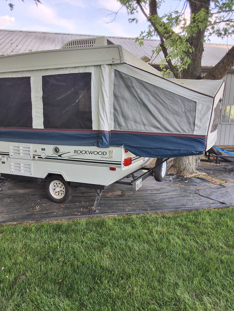 Rockwood Premier pop-up RV rental set up outdoors, nestled beside a tree on black landscape fabric.