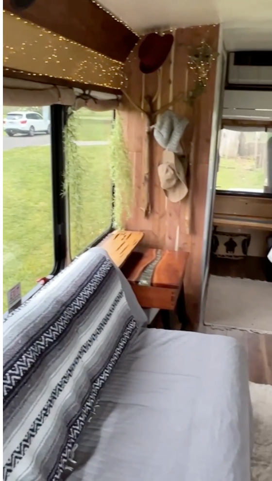 Cozy RV rental interior: rustic wood, string lights, window views, and a comfy bed. Your mobile home awaits! — photo 8