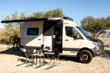 Beige camper van RV rental with outdoor kitchen, dining setup & bike rack, perfect for desert adventures.
