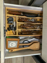 An RV rental kitchen drawer with wooden organizer. Neatly arranged cutlery, cooking tools, corkscrew, and a Pelican Brewing koozie.