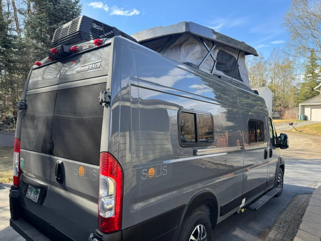 This gray Winnebago Solis camper van with a pop-top roof is ideal for your next rv rental road trip. Exterior shows rear, side, and AC unit.
