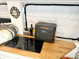 Compact RV rental interior featuring a Jackery power station, Nutrichef induction cooker, and cozy bed setup.