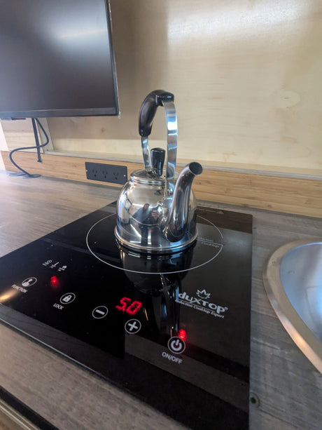 Inside an RV rental: a gleaming kettle sits on a DuxTop induction cooktop, powered on for quick hot water in this compact kitchen.