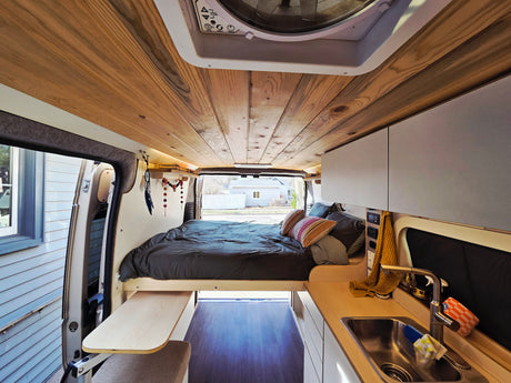 Discover cozy van life in this rv rental. Features a stylish wood-paneled ceiling, comfy bed, and compact kitchenette.