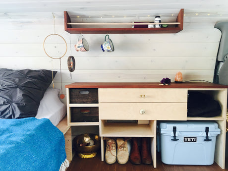 Cozy RV rental interior: Bed, custom storage, & Yeti cooler make van life comfortable.