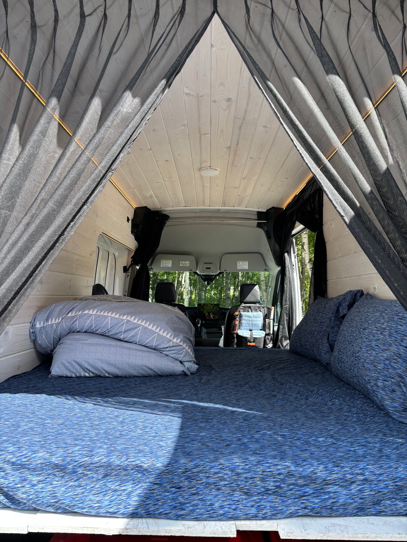 Relaxing rv rental interior: blue bed, wood walls, and mesh bug screen, looking toward the cockpit.