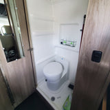 Inside an RV rental: a compact bathroom with a white toilet, integrated shower stall, wood-look doors, and a shower caddy.