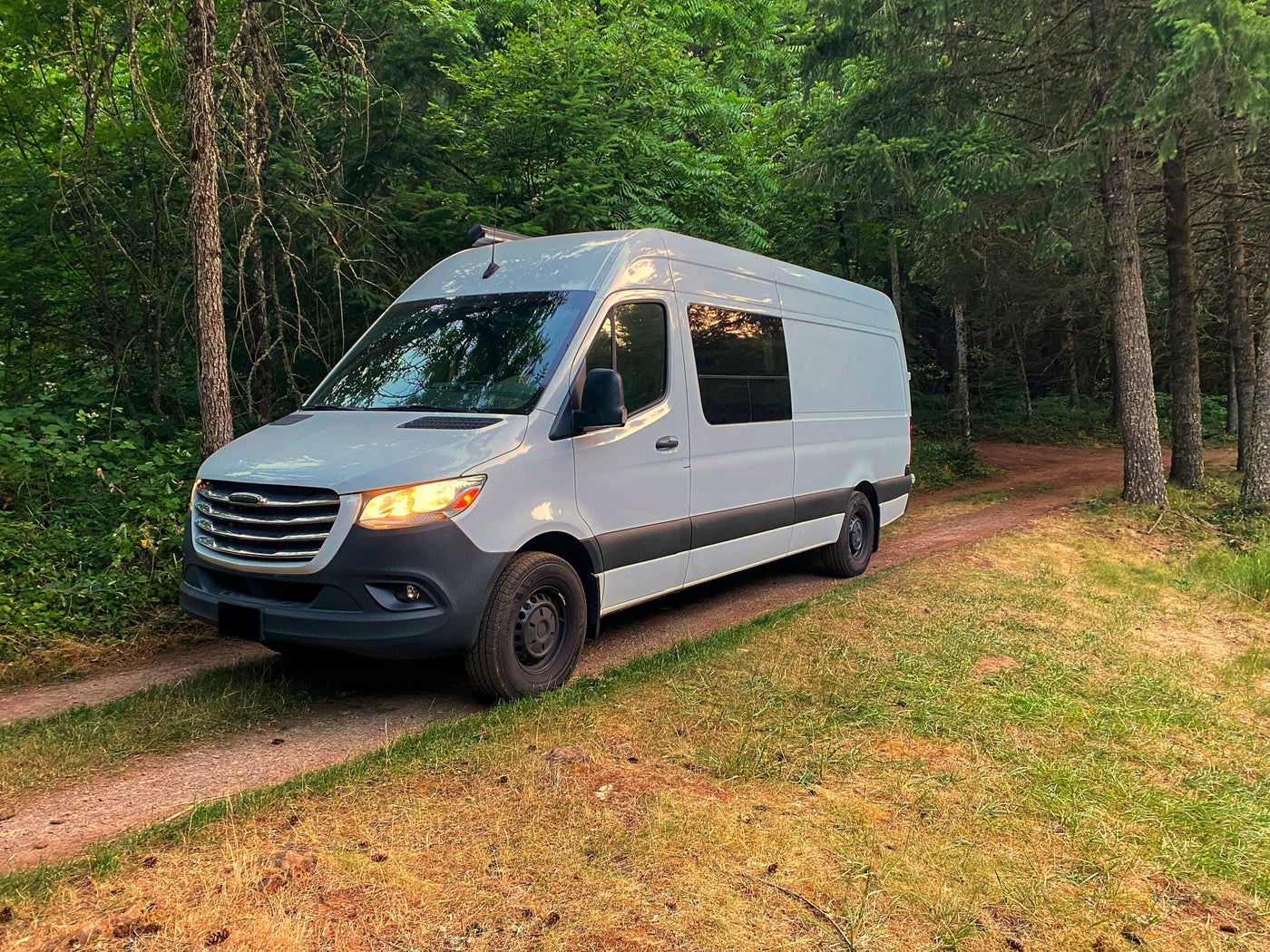  and dinette with refreshing park views. Ideal for travels.|Cozy **RV rental** interior: a well-lit camper van kitchen and living space seen through an open side door with a screen.|White camper van — photo 2