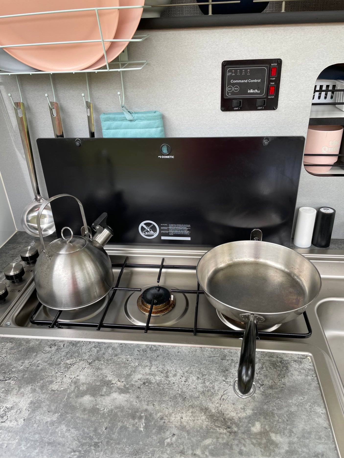 Compact RV rental kitchen showing a Dometic stove, kettle, pan, and inTech Command Control panel for systems.