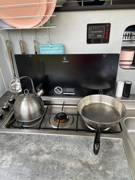 Compact RV rental kitchen showing a Dometic stove, kettle, pan, and inTech Command Control panel for systems.