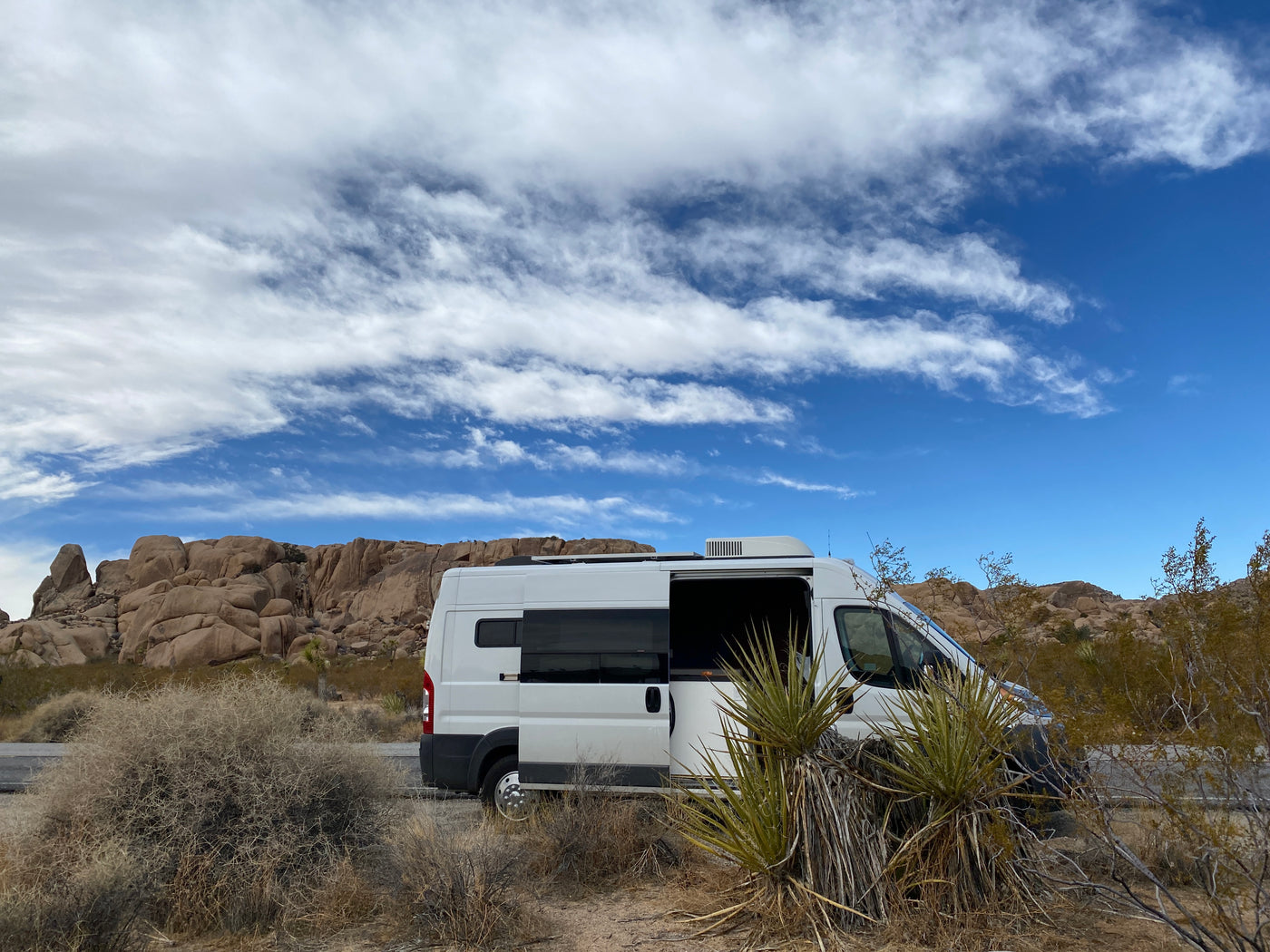 White RV rental parked in a desert landscape with its side door open, surrounded by large rocks and a blue sky. — photo 19