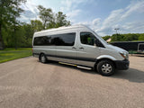 Silver Sprinter van, ideal for RV rental, parked on asphalt with trees and a cloudy sky. Perfect for an adventure.