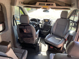 View from rear of Ford Transit RV rental interior. Features front cabin, grey seats, dash, and custom fabric wall panels.