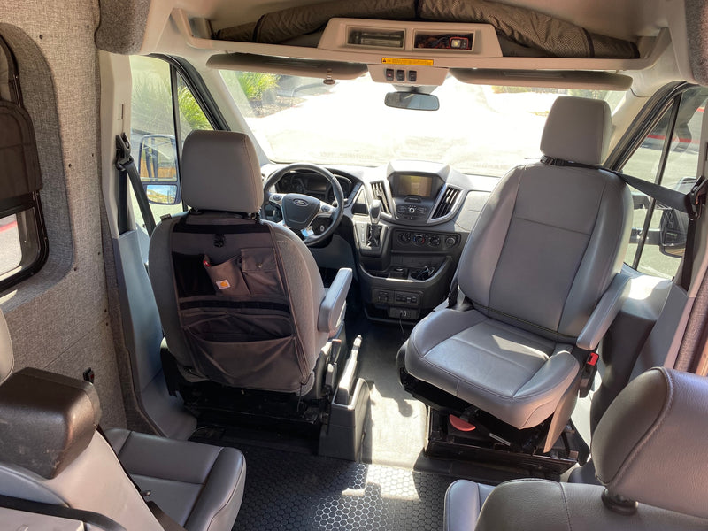 View from rear of Ford Transit RV rental interior. Features front cabin, grey seats, dash, and custom fabric wall panels. — photo 15