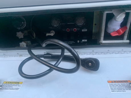 RV rental utility bay showing fresh, gray, and black water tank controls, waste pump, and critical warning labels.
