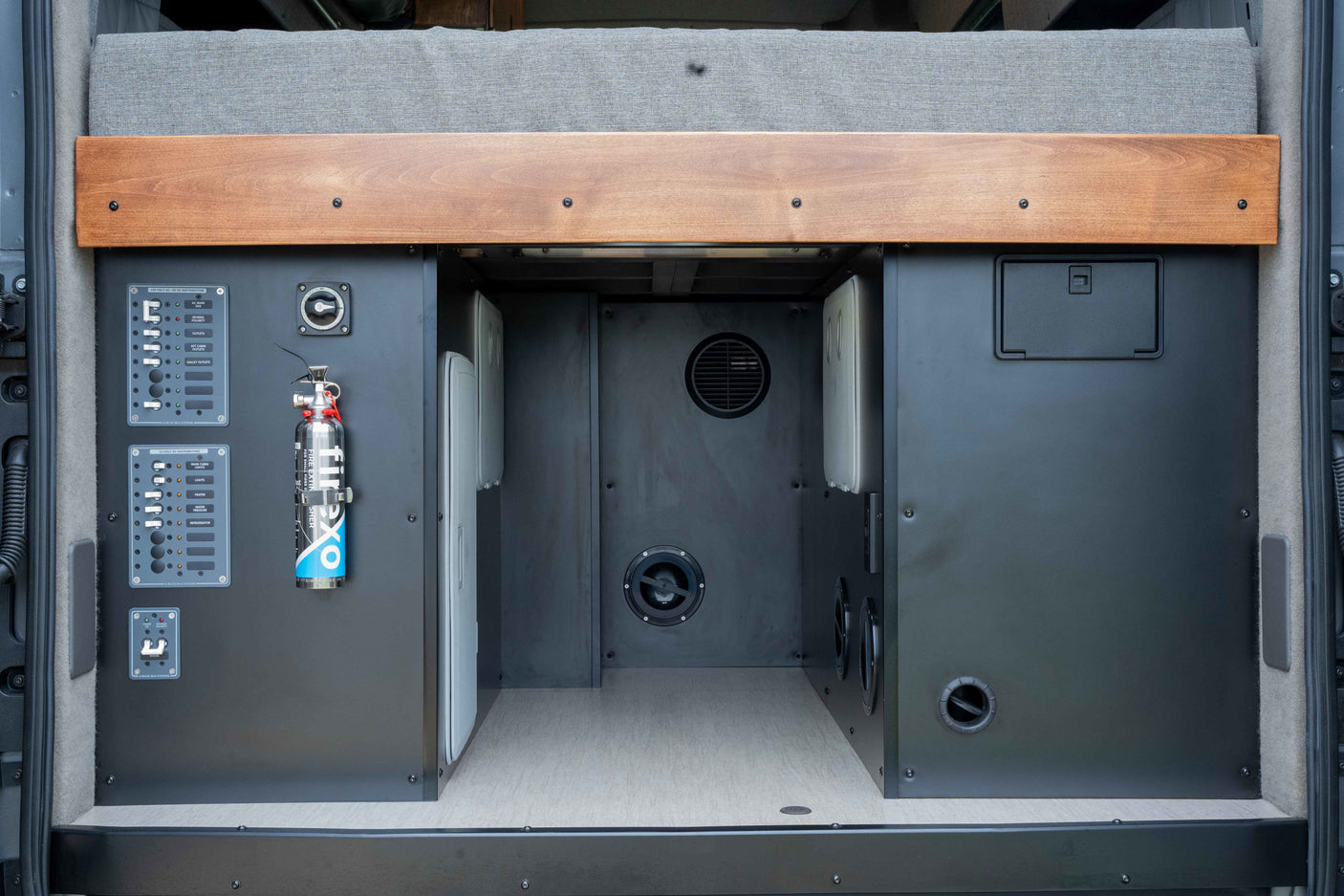 RV rental rear storage in a camper van, showing electrical panels, fire extinguisher, and vents for off-grid living.