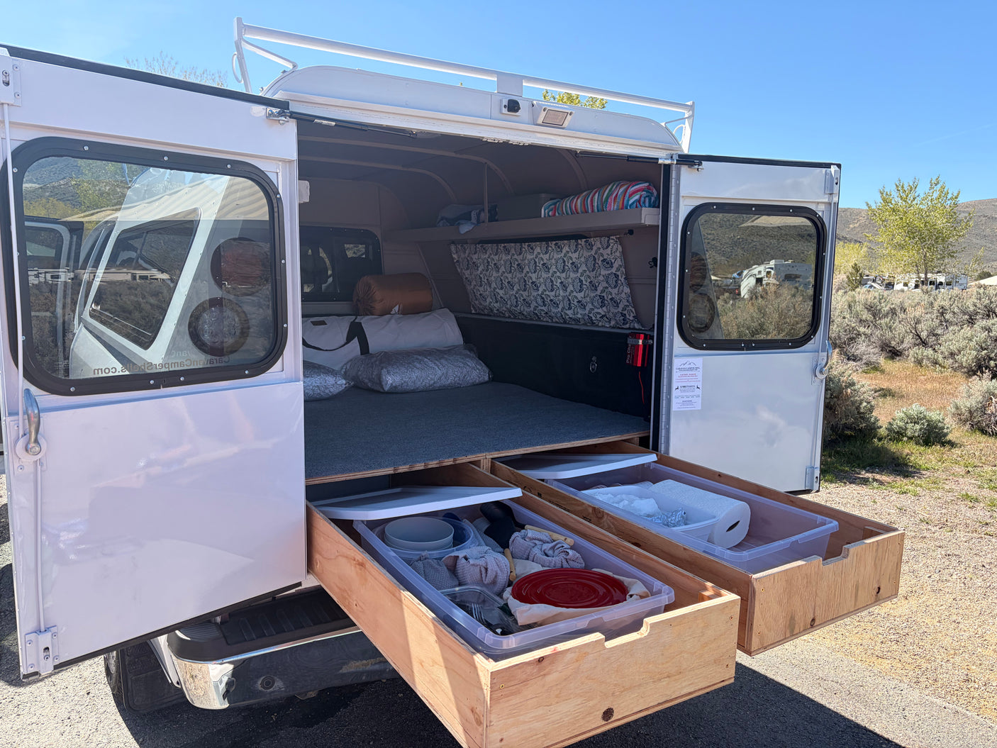 Open rv rental truck camper reveals a bed, pull-out kitchen storage drawers, and roof rack. Ready for your camping adventure!