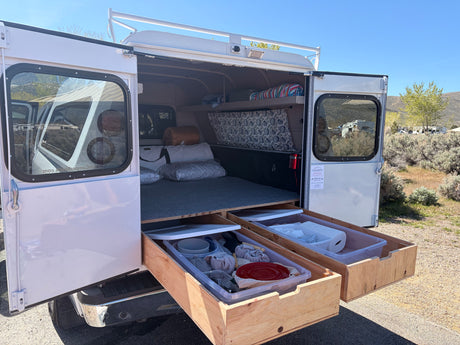Open rv rental truck camper reveals a bed, pull-out kitchen storage drawers, and roof rack. Ready for your camping adventure!