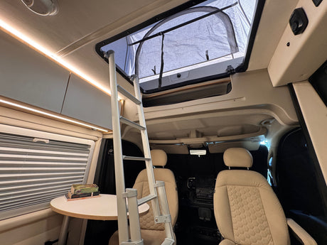 Inside an RV rental: a cozy pop-top camper with ladder access to the sleeping area, front seats, and a table.