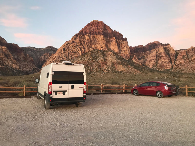 prepped for delicious baking.|Fresh chocolate chip cookies cooling on a wooden board in a compact RV kitchen. Perfect for your next RV rental adventure!|White RV rental van parked on a dirt road amid tall pine trees under clear blue sky — photo 4