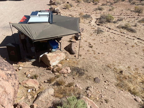 An RV rental in a desert landscape, its large awning providing shade for a comfortable off-grid camp, complete with solar and a dog.