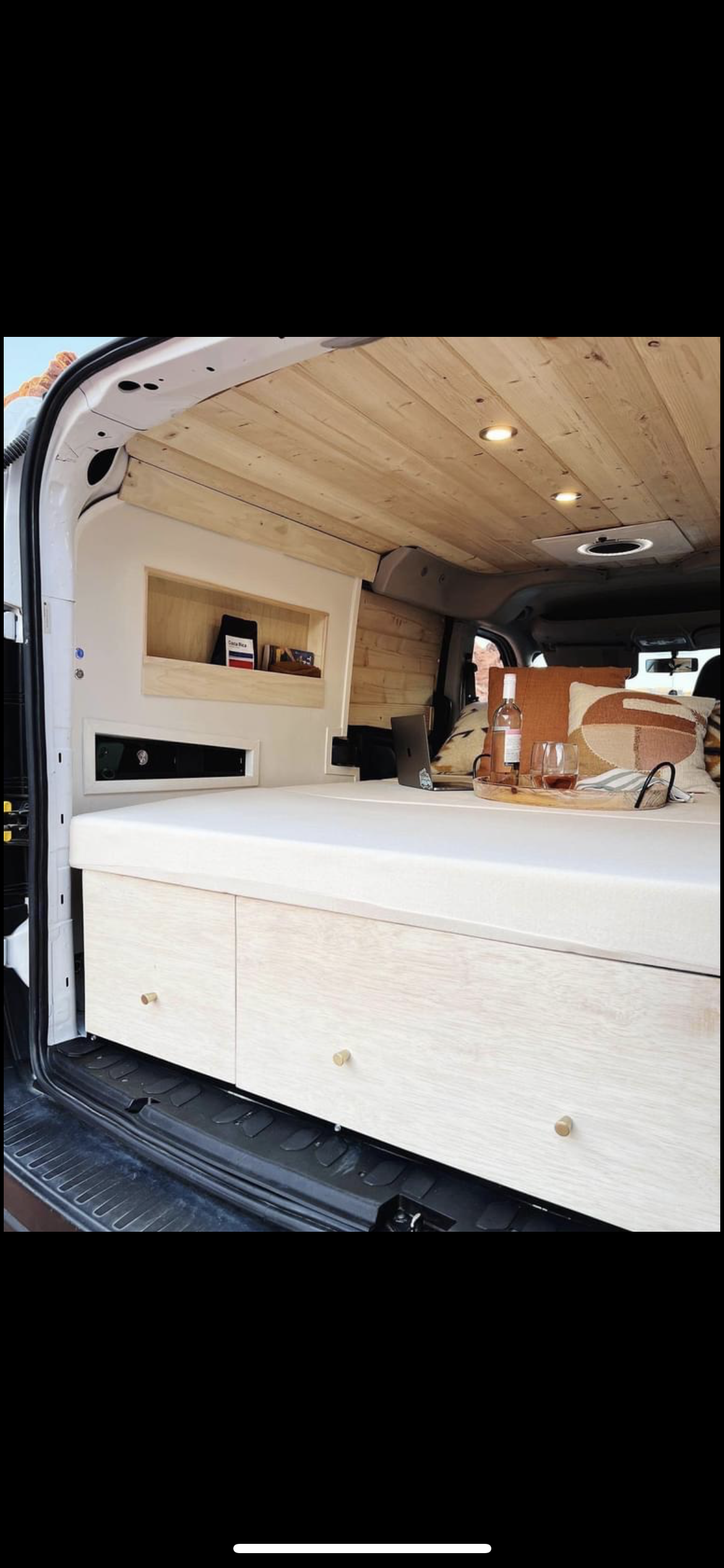 This cozy RV rental features a natural wood ceiling, built-in storage, and a comfy bed. Perfect for van life.