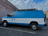 Blue & white service van with roof rack parked by a brick wall. A utility vehicle for work, not an RV rental journey.
