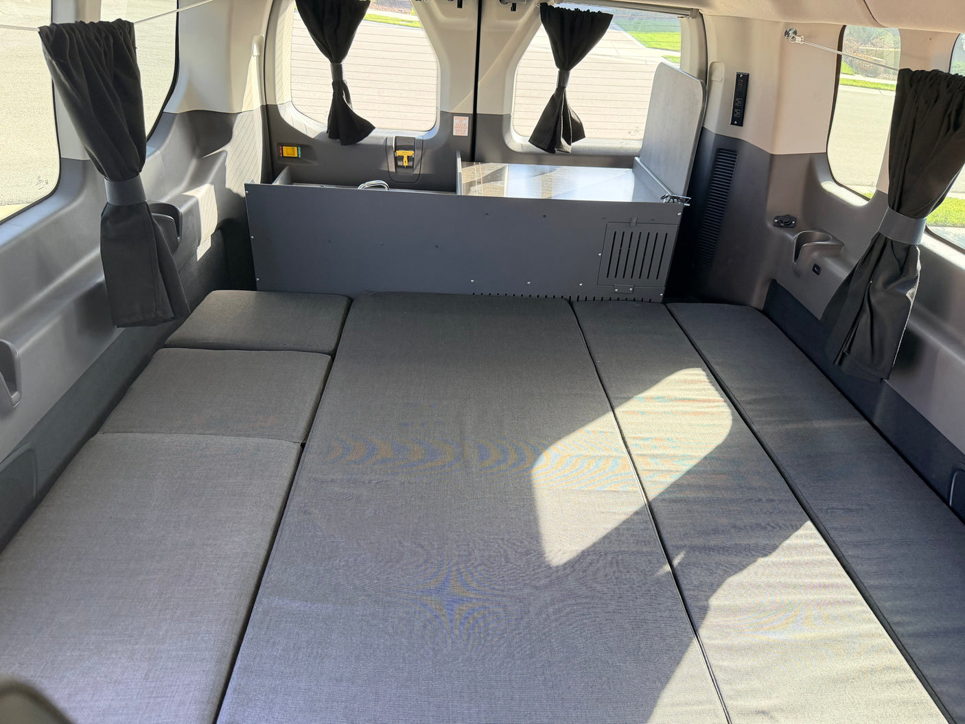 RV rental camper van interior with modular bed, kitchen unit, and curtains.